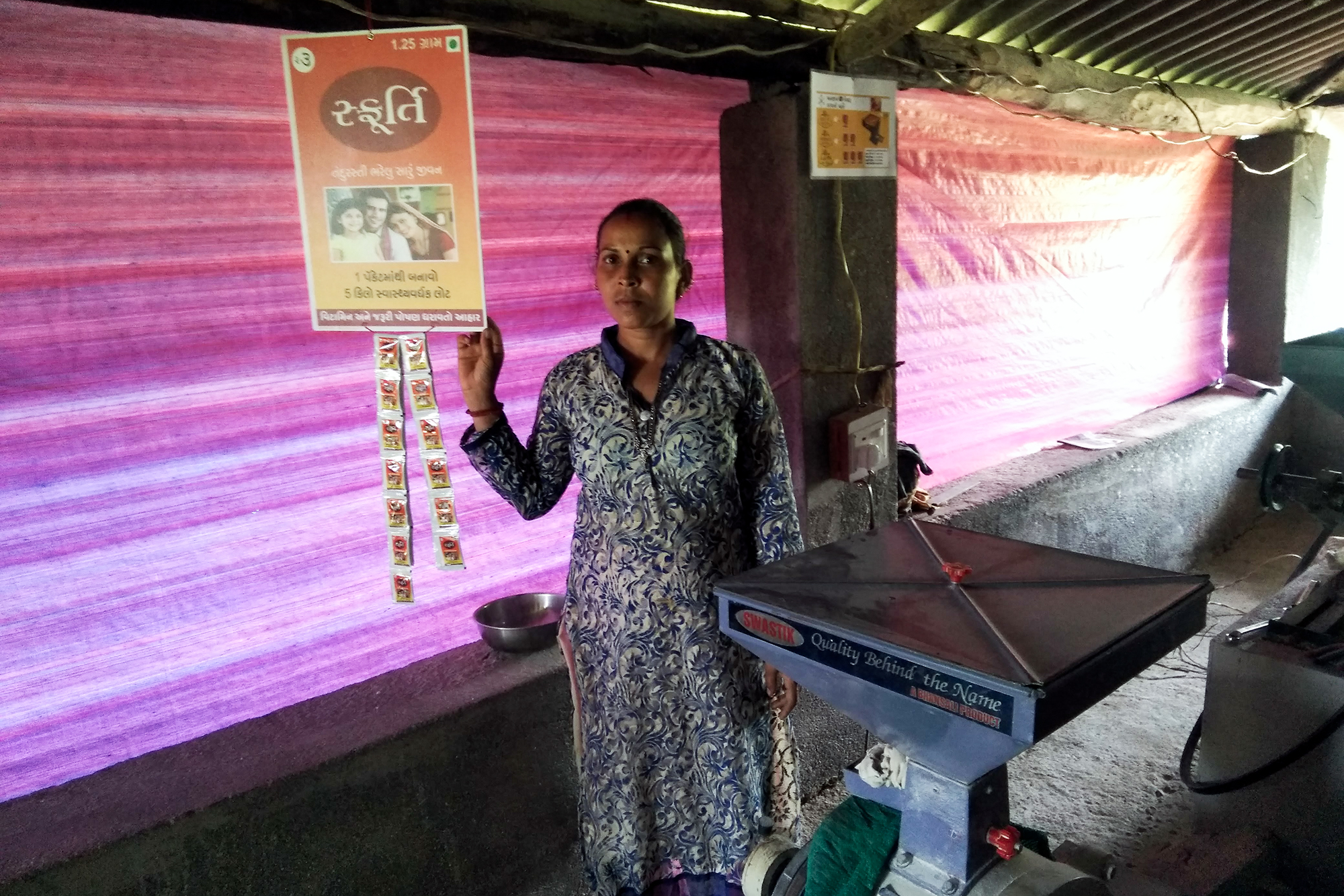 A woman holding a Sfurti sign next to a flour mill