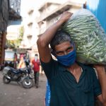 A laborer in a mask carrying a sack full of Lady Finger (Bhindi) vegetables at a wholesale vegetable market