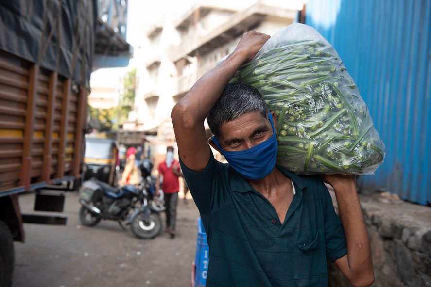 A laborer in a mask carrying a sack full of Lady Finger (Bhindi) vegetables at a wholesale vegetable market