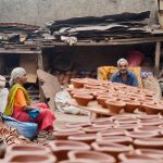 An older man and woman sit amongst stacked potter