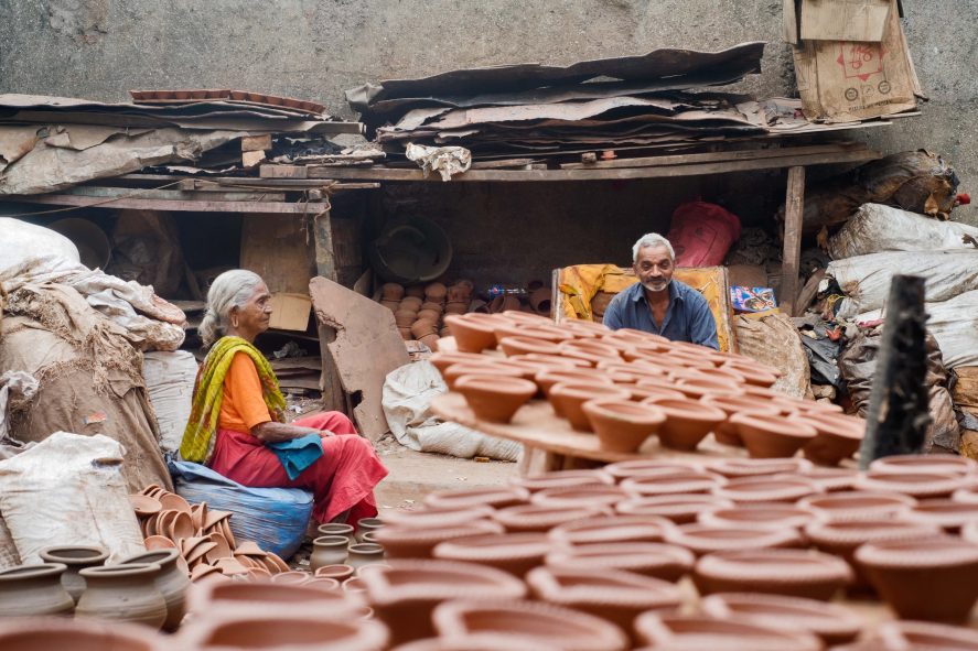 An older man and woman sit amongst stacked potter