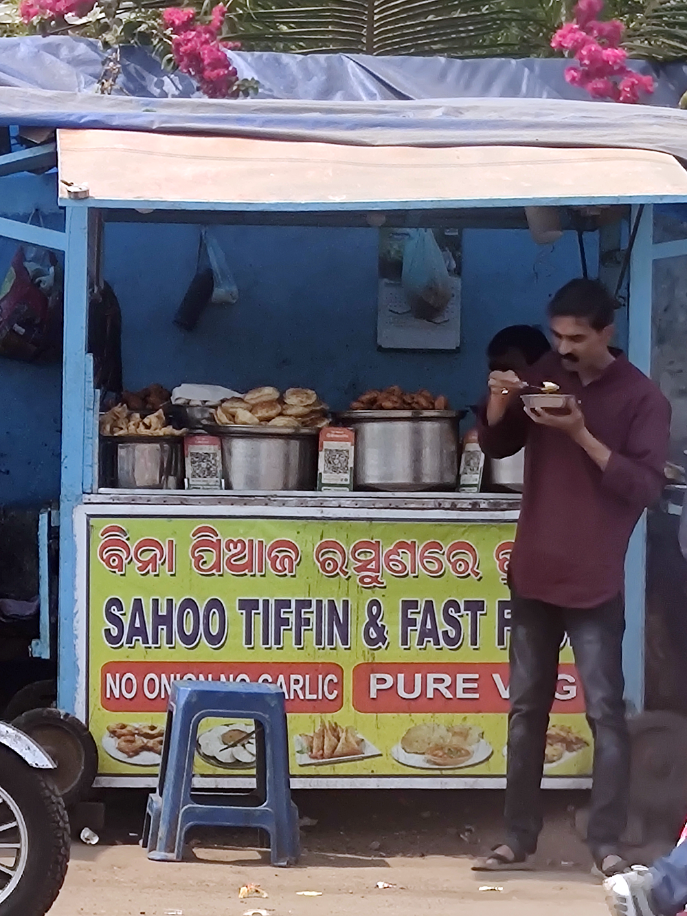 A man eats in front of a food cart that has QR codes for digital payment