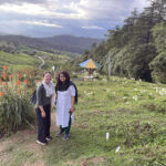 Grace Catherine Dunham and Pallavi Rajkhowa pose in front of flowers and farmland.