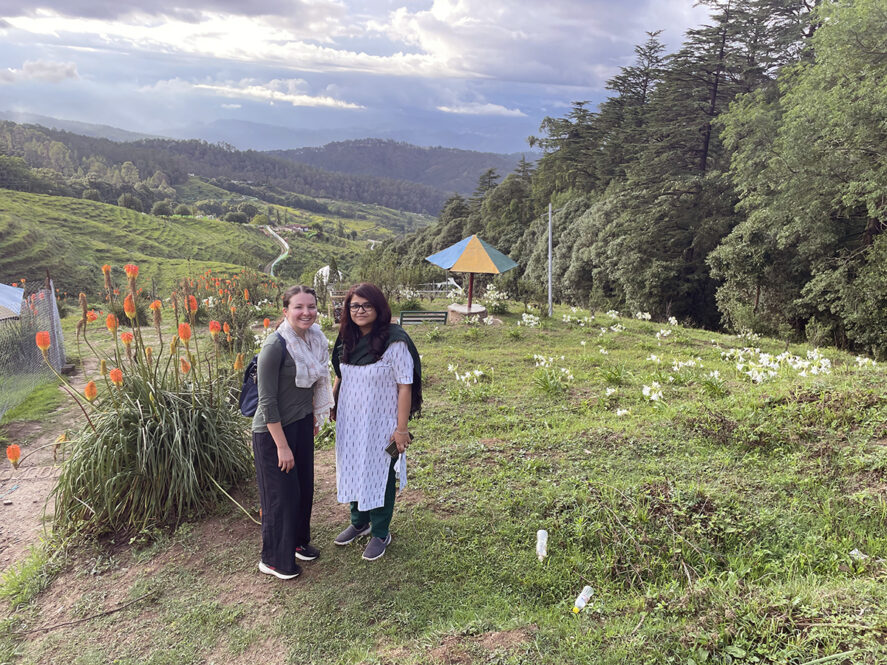 Grace Catherine Dunham and Pallavi Rajkhowa pose in front of flowers and farmland.