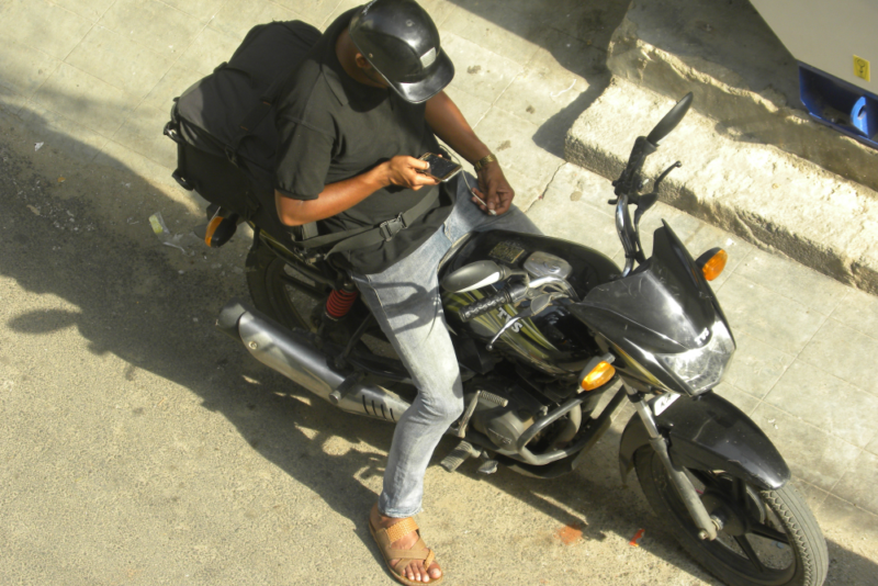 A delivery worker sitting on his motorcycle and looking at his phone