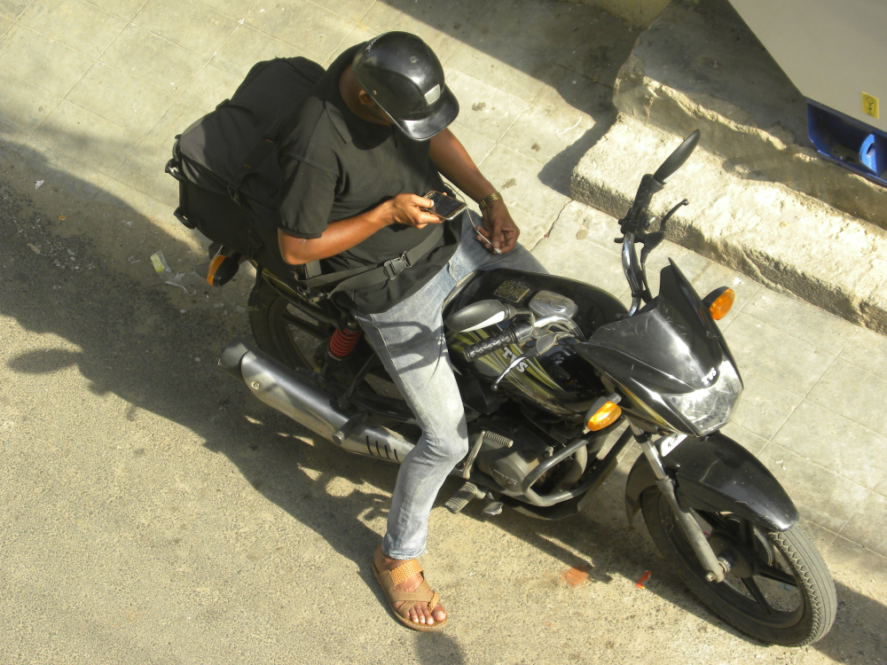 A delivery worker sitting on his motorcycle and looking at his phone