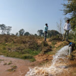 Two men standing by a water pump