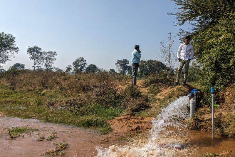Two men standing by a water pump