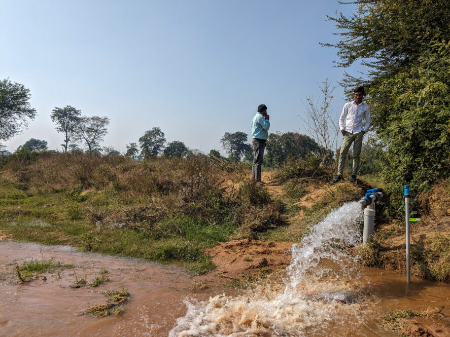 Two men standing by a water pump