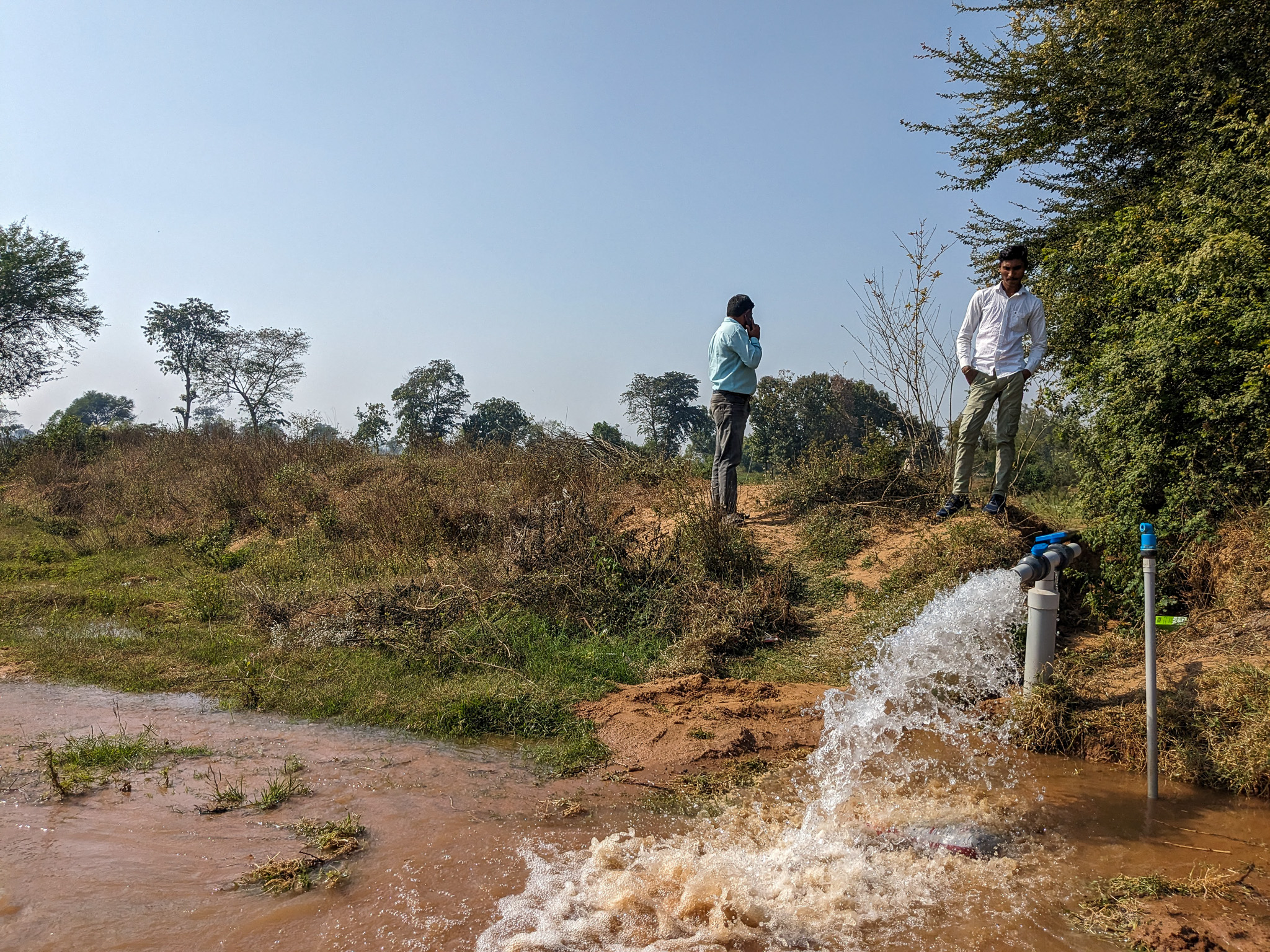 Two men standing by a water pump