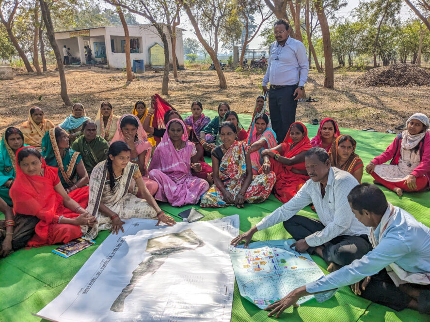 Researchers and female farmers sit on a green tarp during a focus group discussion.