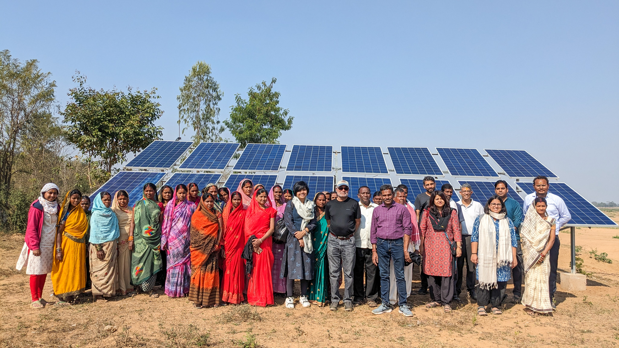 TCI and PRADAN staff posing with farmers in front of solar panels