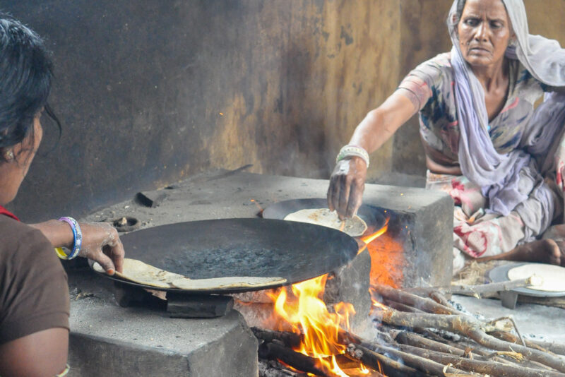 Two women cooking flatbreads in a pan over an open fire