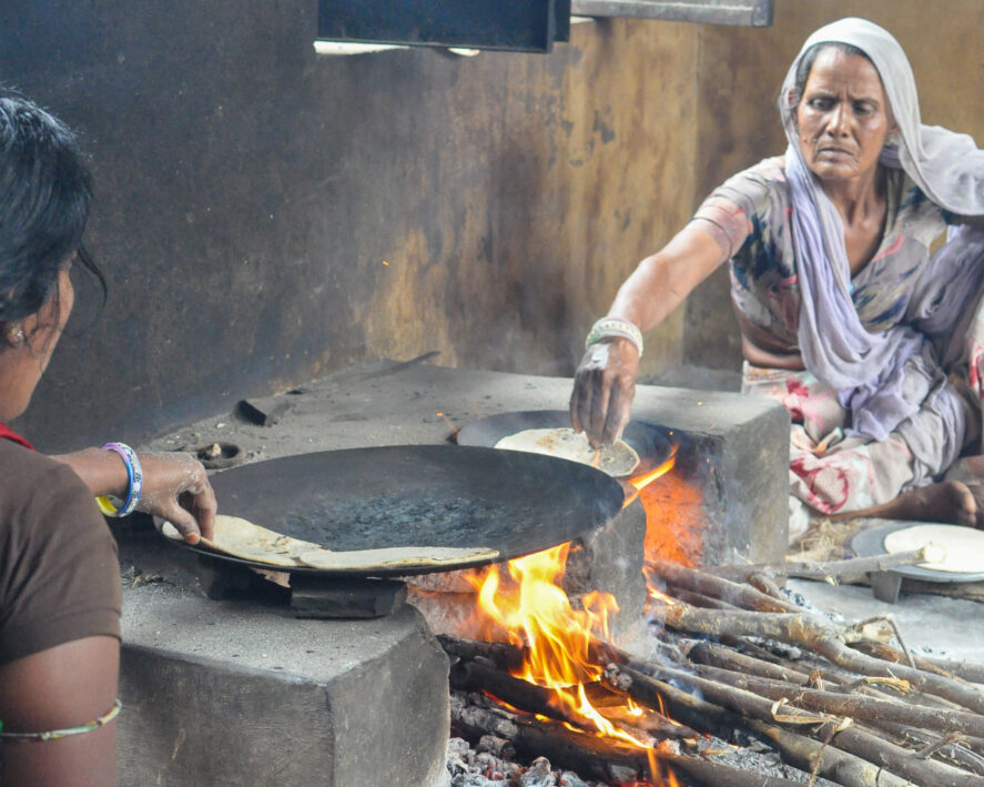 Two women cooking flatbreads in a pan over an open fire