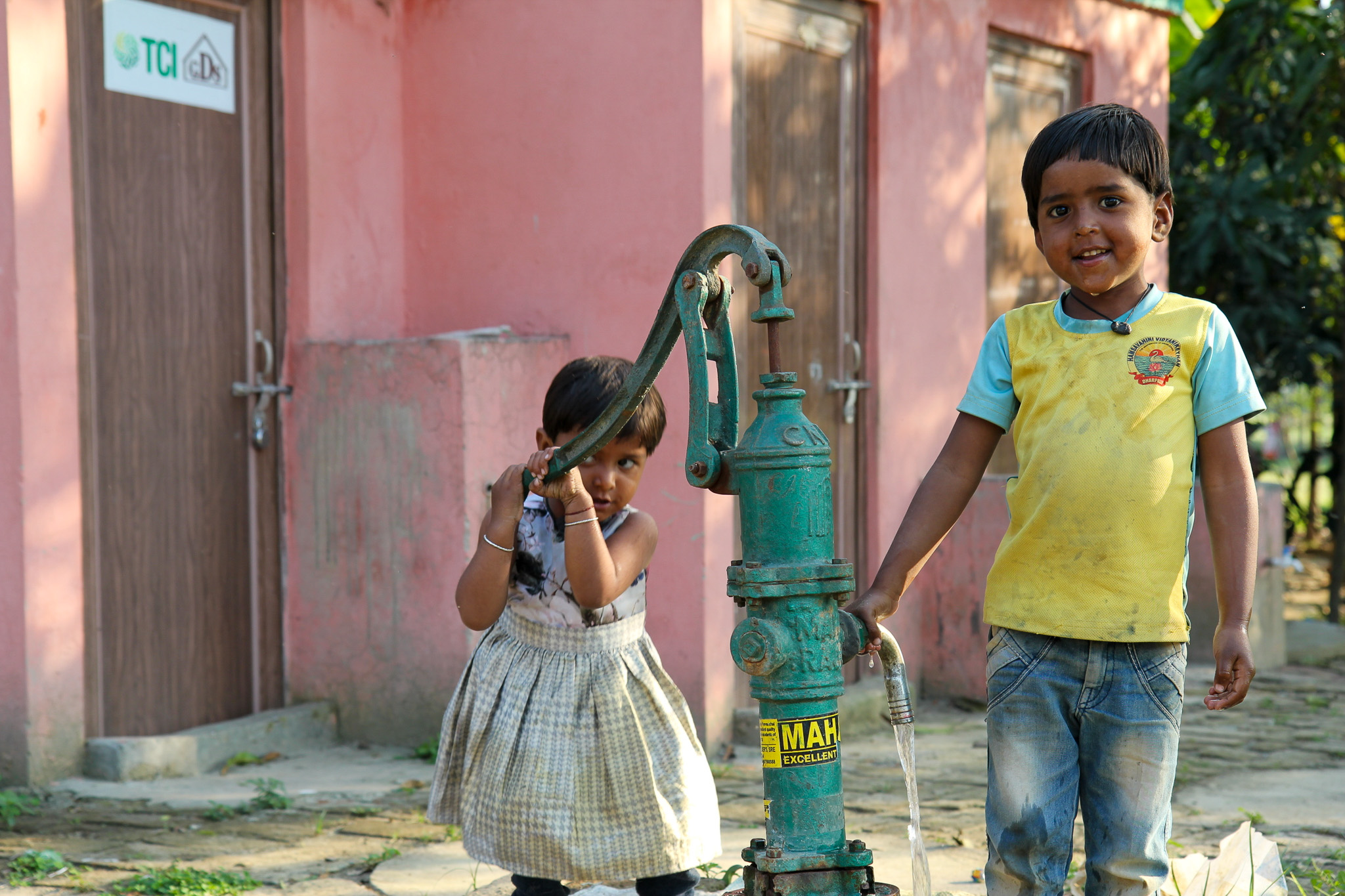 A young boy and girl standing by a water pump