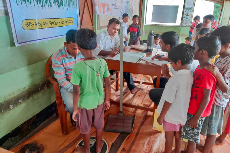 A doctor weighing a child on a scale as more children wait their turn
