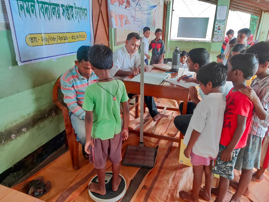 A doctor weighing a child on a scale as more children wait their turn