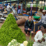 Jocelyn Boiteau sitting next to a pile of green vegetables at a market