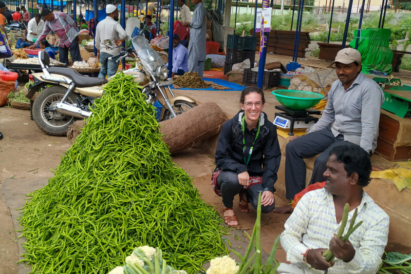 Jocelyn Boiteau sitting next to a pile of green vegetables at a market