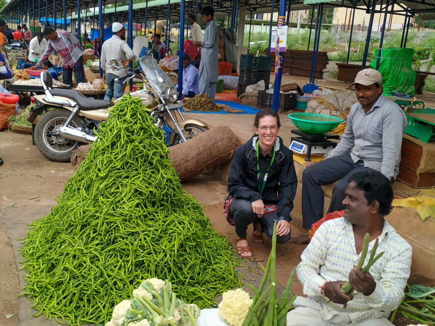 Jocelyn Boiteau sitting next to a pile of green vegetables at a market