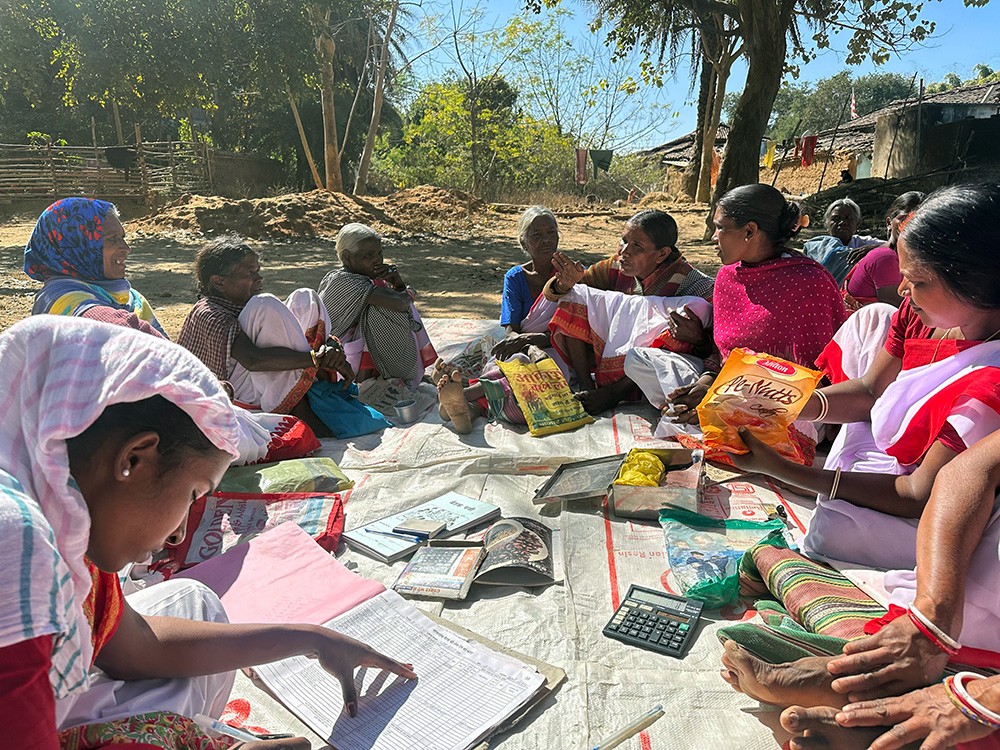 Women sit in a circle outside for a self-help group meeting