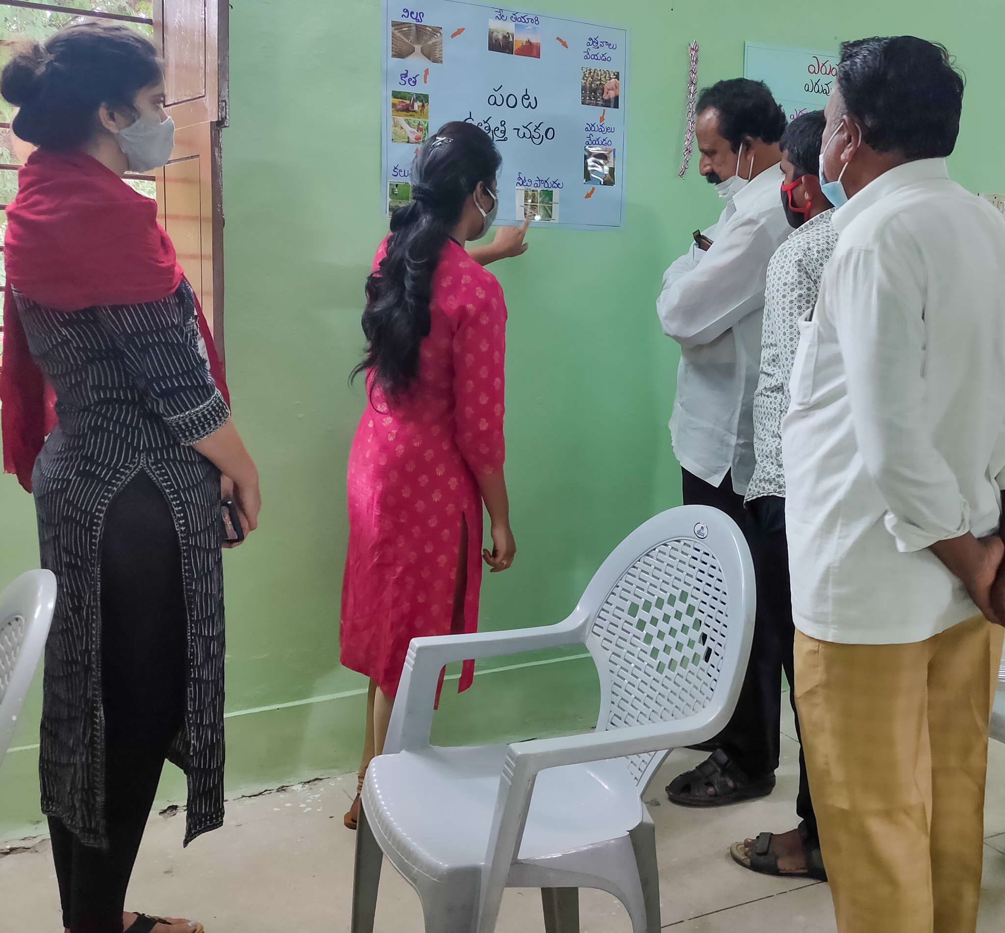 Vanisha Sharma standing in a room with a woman and several men looking at a poster on the wall