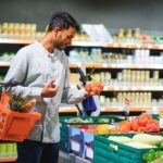 A man shopping in a supermarket picking up red tomatoes