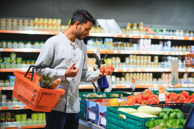 A man shopping in a supermarket picking up red tomatoes