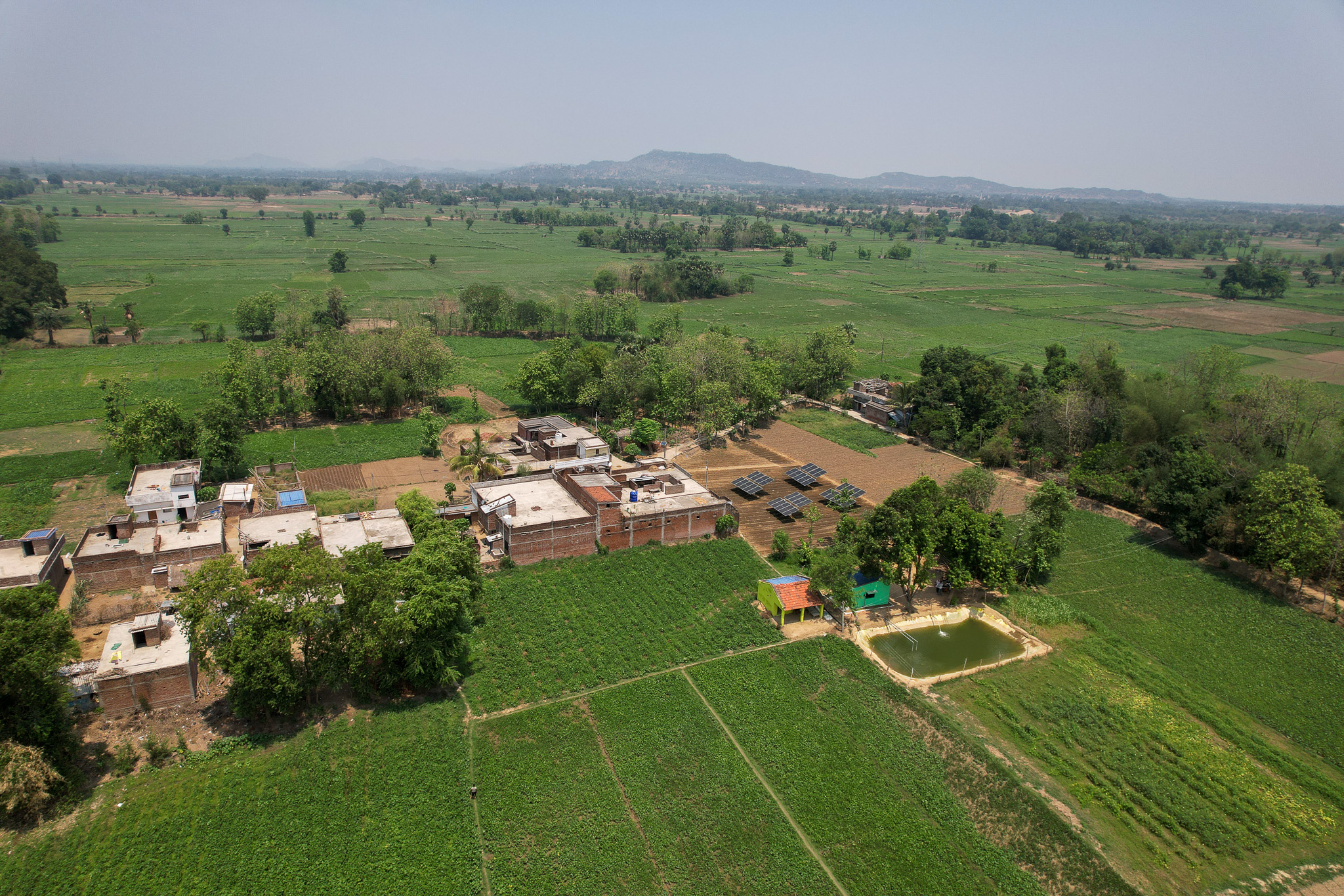 A bird's eye view of an agrivoltaics installation, with solar arrays and an irrigation pond surrounded by farms.